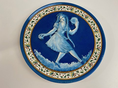 Fransk fajance tallerken / platte med motiv af blå pige med lange fletninger i relief. Pigen danser og spiller musik med kastagnetter og tamburin, første halvdel af det 20. århundrede