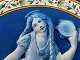 Fransk fajance tallerken / platte med motiv af blå pige med lange fletninger i relief. Pigen danser og spiller musik med kastagnetter og tamburin, første halvdel af det 20. århundrede